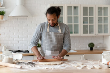 Focused young African American man baking cookies in home kitchen. Food blogger, baker, chef in...
