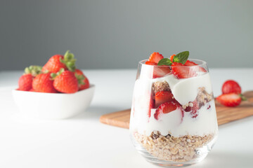 Glass with granola, yogurt and fresh strawberries on white table. Healthy breakfast bowl concept.