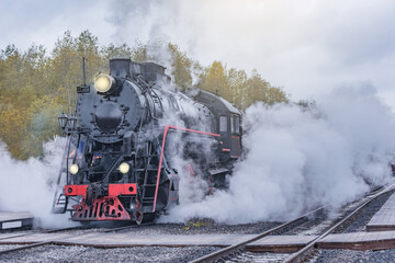 Fototapeta na wymiar Retro steam train departs from the station wooden platform at cloudy evening.