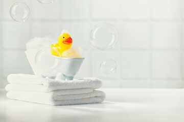 A miniature bubble bath, yellow rubber duck and white towels on bathroom countertop, children bath...