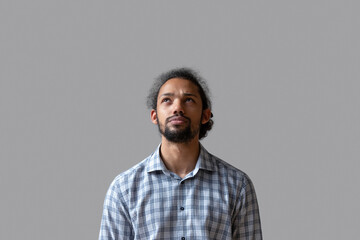 Serious young Black guy in casual standing isolated at grey background, looking at copy space over...