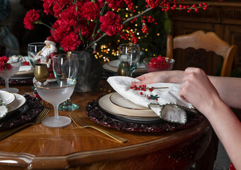Hands setting and decorating dining table with napkin and ornament for Christmas and New Year holidays.