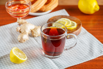 strong tea a cup on the table next to ginger lemon, donuts with cream on a napkin.