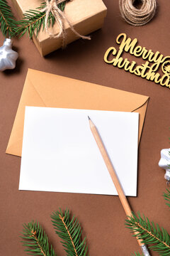 Blank white Christmas card template on beige background. Fir branches, holiday decorations, pencil, lfat lay. Eco christmas