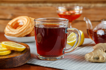 On the table is a cup of strong tea with lemon and ginger, donuts and jam in a vase.