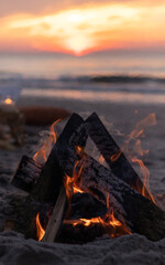 A fire with a red flame is burning on a sandy beach on the shores of the Baltic Sea. Sunset picnic with bonfire.