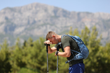 Tired man traveler putting his head on walking sticks against backdrop of mountains
