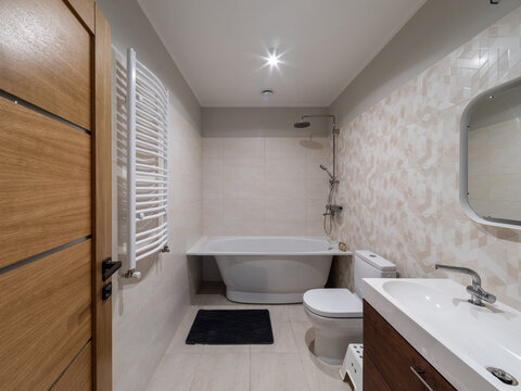 Modern interior of bathroom. White sink, toilet, bath. Wooden door.