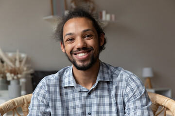 Happy millennial African American hipster guy looking at camera with toothy smile. Young business man in casual, blogger, coach, teacher giving training, making video call at home. Head shot portrait
