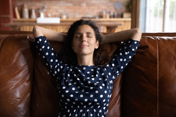 Serene rest. Peaceful young latina female relax on comfy couch alone with hands over head keep eyes...