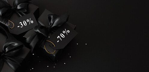 Top view of gift black boxes with satin ribbons and bows and discount tags on black background, copy space. Black Friday Sale template.