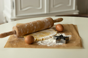 The dough, eggs and flour prepared for cooking lie on parchment paper, next to it lies a wooden...