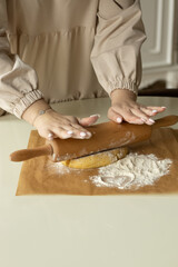 A girl rolls out the dough on parchment paper sprinkled with flour with a wooden rolling pin.