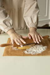 A girl rolls out the dough on parchment paper sprinkled with flour with a wooden rolling pin.