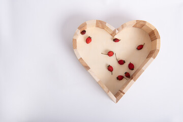 Wooden heart with red dried berries on an isolated gray background with shadow