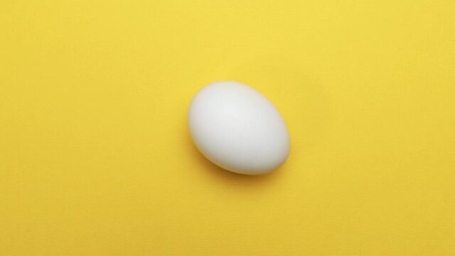 There is a white chicken egg on a yellow background. It starts spinning faster and faster.