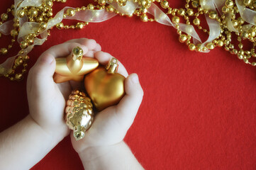 children's hands hold golden spruce toys on a red background. Preparing for a Merry Christmas and a Happy New Year. winter holidays.