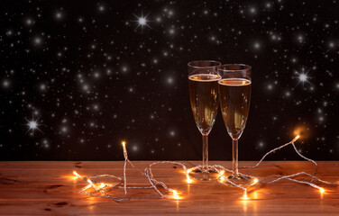Glasses with champagne and glowing christmas lights on dark background. Selective focus.