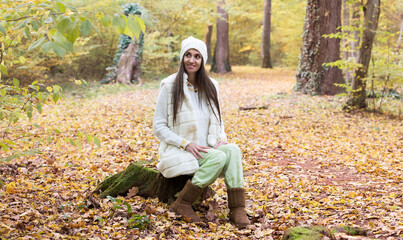 Attractive woman sitting on a tree stump in forest with colorful autumn leaves