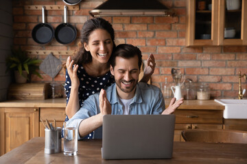 Wonderful proposal. Excited family couple laugh splash hands by pc receive online offer to buy...
