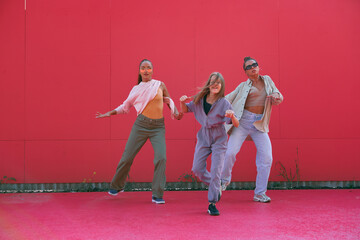 Dancing girls perform energetic street dance having fun on red background outdoors. Professional hip hop female dancers