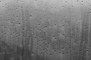 Raindrops on the window pane on a gray background. Natural pattern of raindrops. Texture for creativity. Water on the surface of the glass.