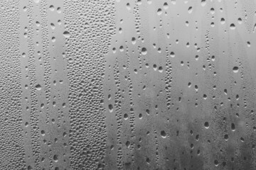 Raindrops on the window pane on a gray background. Natural pattern of raindrops. Texture for creativity. Water on the surface of the glass.