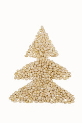 Pine nuts are laid out on a plain craft background in the shape of a Christmas tree. Christmas style.