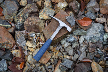 Steel geologist rock pick over brown and grey rocks in mining area rich with chromite ore in...