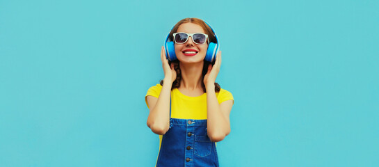 Portrait of happy smiling young woman with headphones listening to music on a colorful blue background