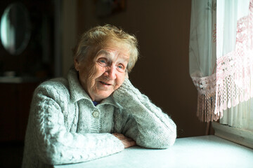An old woman sits in the her house near the window.