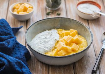 Corn porridge with cheese and sour cream sauce in a gray plate on a wooden background. Georgian cuisine.