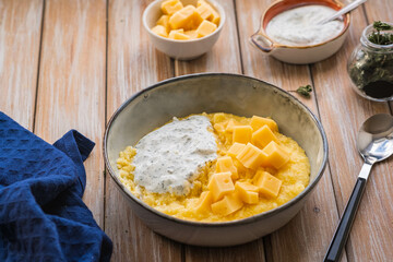 Corn porridge with cheese and sour cream sauce in a gray plate on a wooden background. Georgian cuisine.