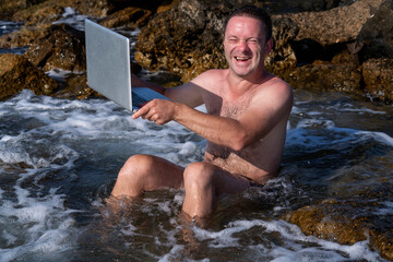 Humorous image of process of cleaning computer notebook. Young man working with laptop on vacation in the sea.