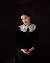 Girl in a historical dress sitting wirh red apple in hands. Studio portrait