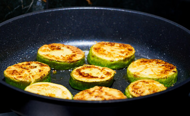 zucchini are fried in a skillet in the kitchen