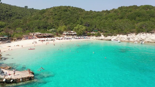 Aerial view moving back of Vrika beach and people sunbathing at Antipaxos island Greece