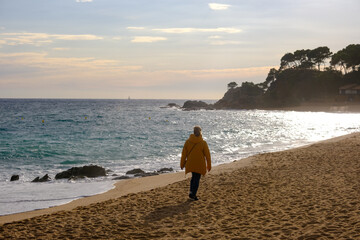 lone unrecognizable woman walk along sea beach in evening sunlight autumn or winter season