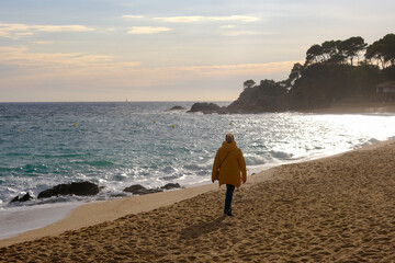 Fototapeta na wymiar lone unrecognizable woman walk along sea beach in evening sunlight autumn or winter season