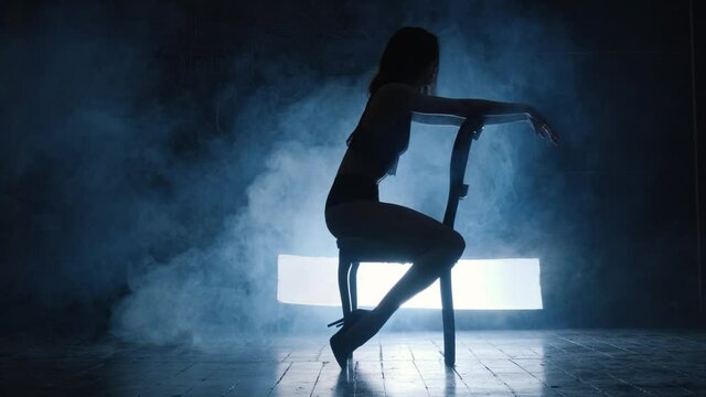 Silhouette of a sexy girl dancing an erotic sensual dance in blue smoke.