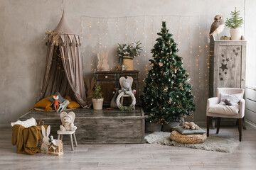 Interior of a children's room decorated for Christmas. Awning bed with toys and pillows, a tree, a wardrobe and an armchair in gray beige colors