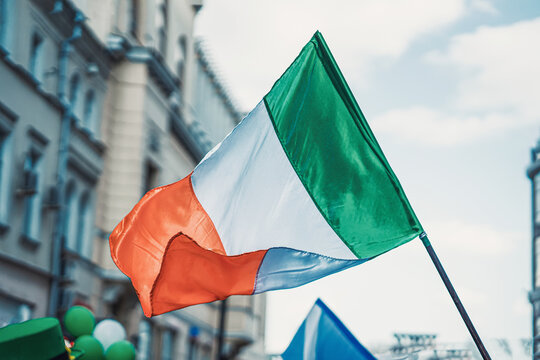 Flag of Ireland close-up on background of sky, city street. Saint Patrick day holiday - Powered by Adobe