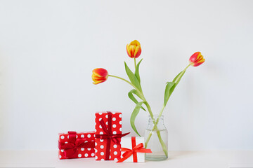 A vase with a bouquet of beautiful tulips and gift boxes on the table. Greeting card for Valentine's Day, March 8, Mother's Day