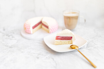 White and pink cake on a plate on a light marble table and a glass coffee mug. Background for Valentine's Day