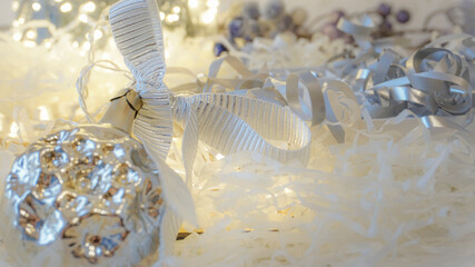 Festive picture of silver Christmas decoration with bow and fairy light bulbs blurred on the background. Composition include warm light colours and is perfect for postcard or as wallpaper.