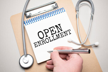 White notepad with the words open enrollment and a stethoscope on a blue background. Medical concept