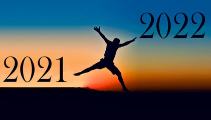 
Silhouette of a young man jumping between 2021 and 2022 against the backdrop of a sunset. happy new year 2022.