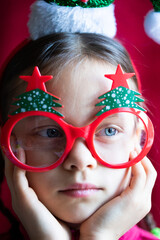 Portrait of funny little serious girl in Christmas glasses and headband of Santa Claus 