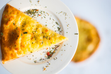 Georgian khachapuri with cheese and spices on the white plate on the white table