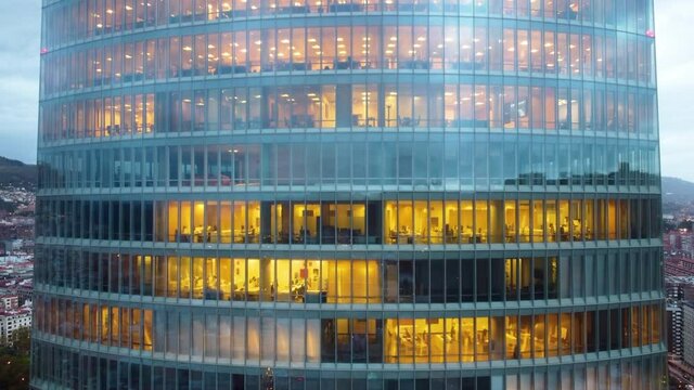 Office style concept. Working hours in the office building at night. Drone flight around the office skyscraper.